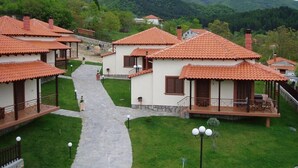 A row of traditional-style cottages with red-tiled roofs, a central pathway, and a mountainous backdrop. - Karyon Apartments (Xanthi)
