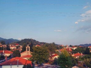 A village with red-roofed houses, a church with a bell tower, and mountains in the background.