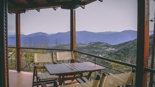 A wooden deck with a table and chairs overlooking a mountainous landscape. - Karyon Apartments (Xanthi)