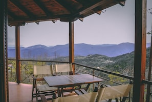 Eine Holzterrasse mit Tisch und Stühlen mit Blick auf eine gebirgige Landschaft.