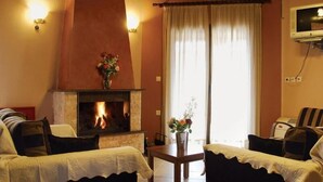 A cozy room with a fireplace, two sofas, a table, and a TV. - Karyon Apartments (Xanthi)