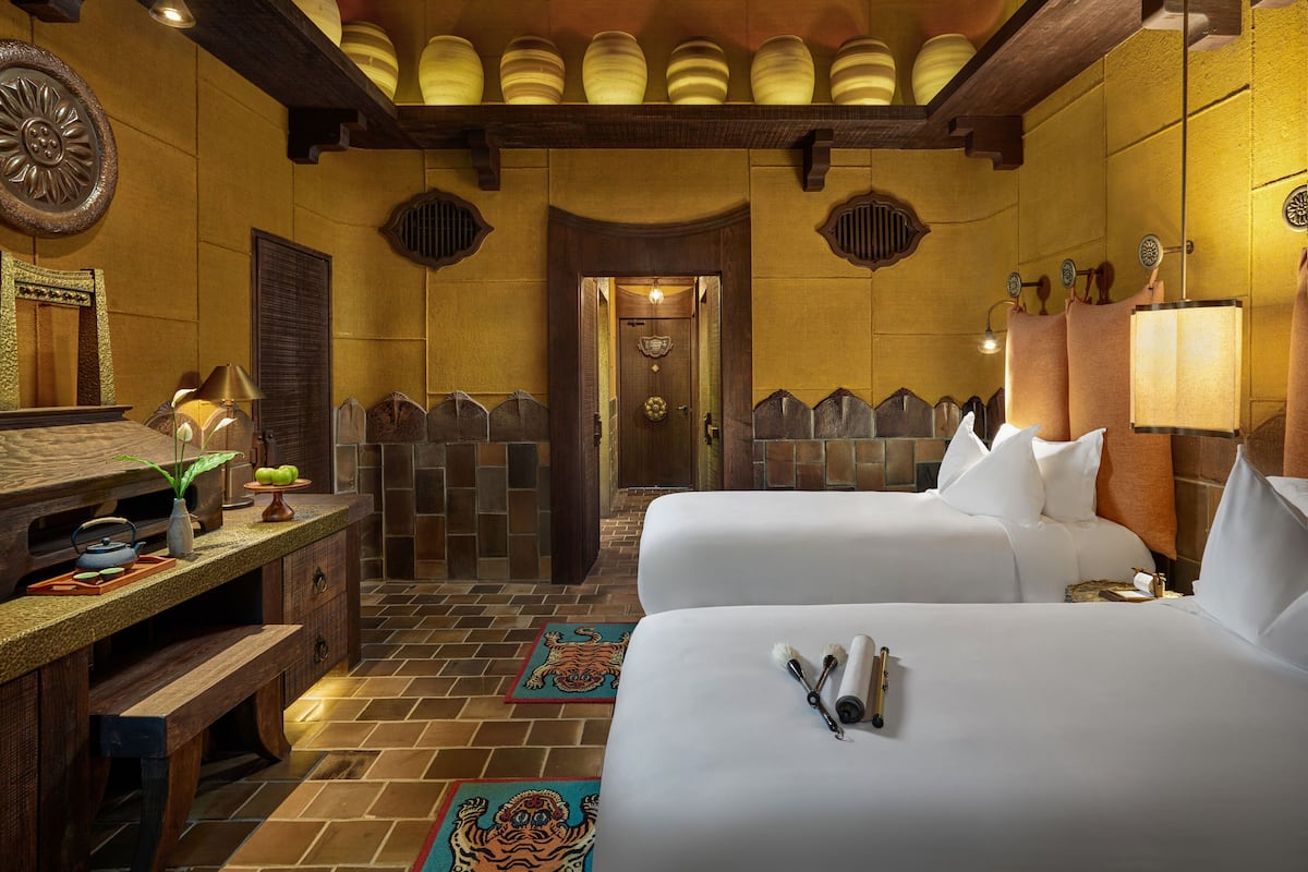 Ein Hotelzimmer mit zwei Betten, einem Holztisch, einem Spiegel und einer Tür zum Badezimmer.