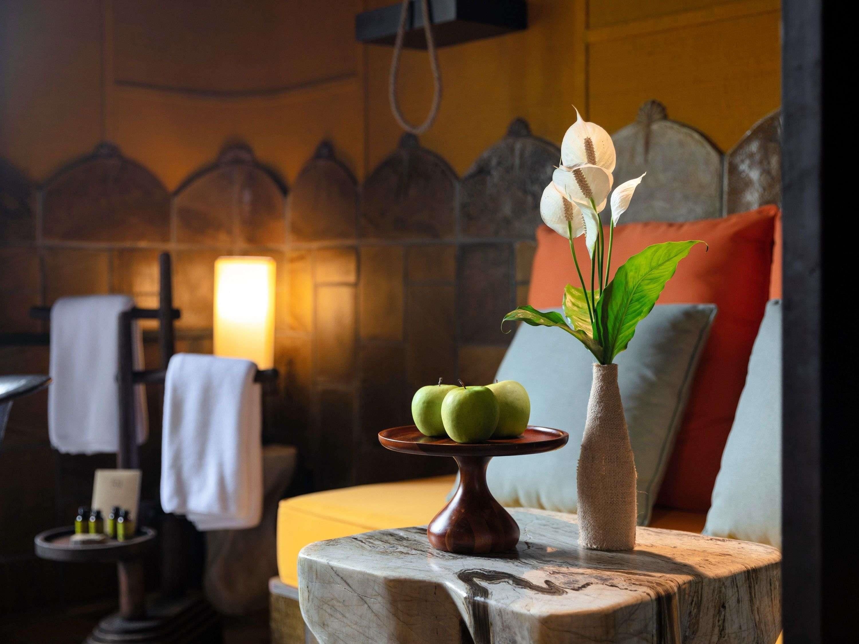 A room with a wooden headboard, a vase with green apples and white flowers, and a small table with a candle.