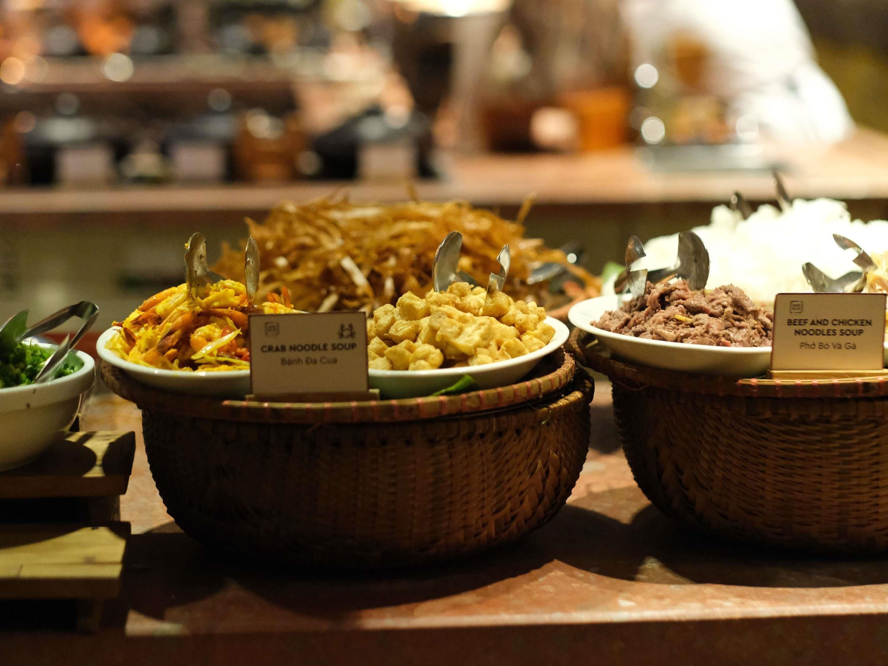 A buffet with labeled dishes including crab noodle soup and beef and chicken noodles soup.