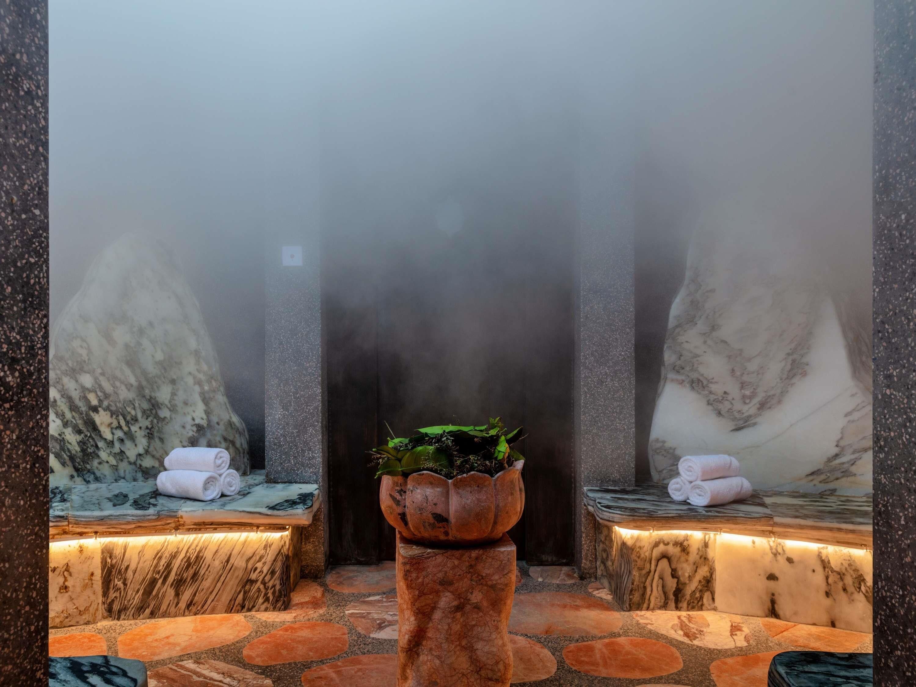 Un espace de détente avec des sièges en marbre, une plante centrale et une atmosphère brumeuse.