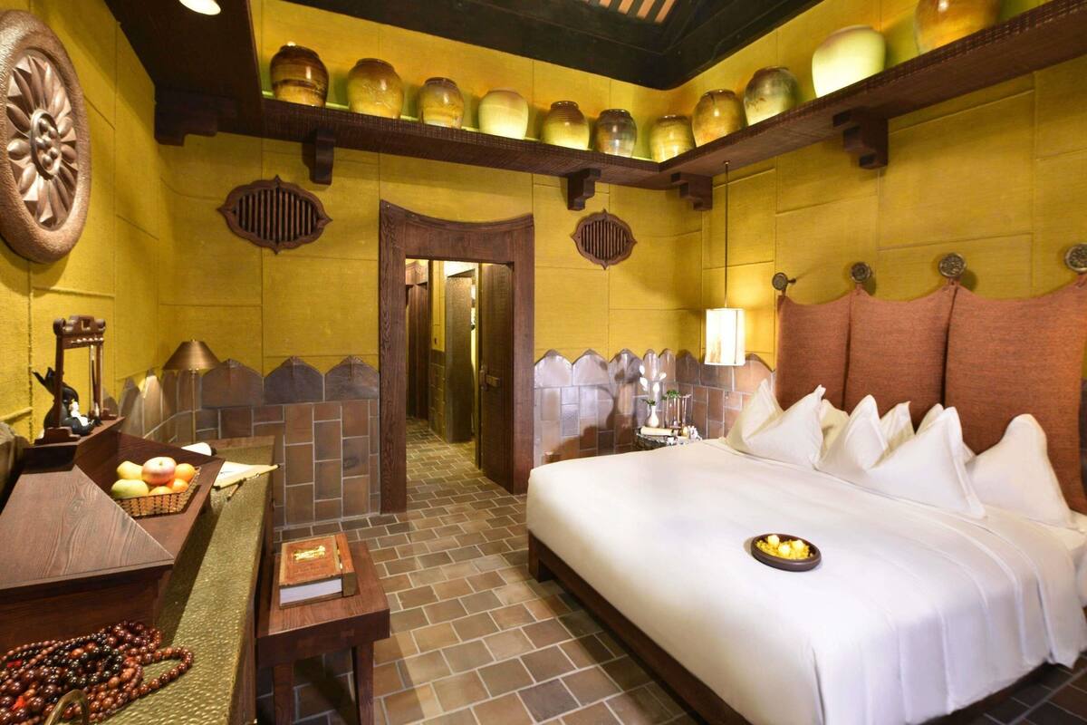Ein Hotelzimmer mit Bett, Schreibtisch, Stuhl, Lampe und einer Wand mit dekorativen Gläsern.