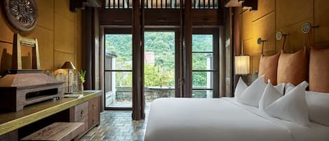 Une chambre spacieuse avec un grand lit, des meubles en bois et une vue sur la verdure grâce à de grandes fenêtres.