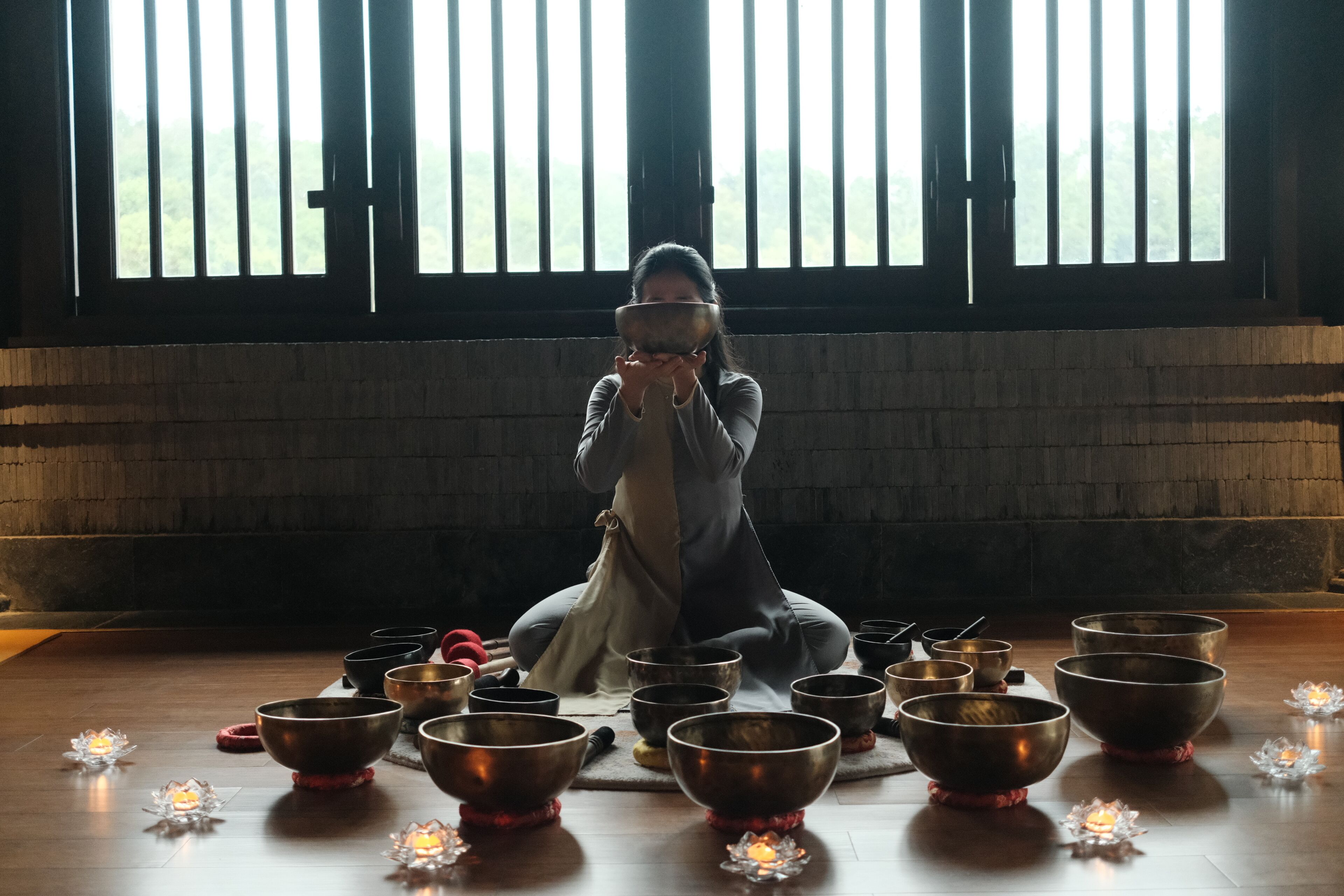 A person sitting on the floor surrounded by several large bowls, with candles placed in front of them.
