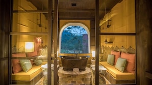 Una spa con una vasca da bagno indipendente, posti a sedere imbottiti e un'ampia finestra ad arco che si affaccia su alberi.