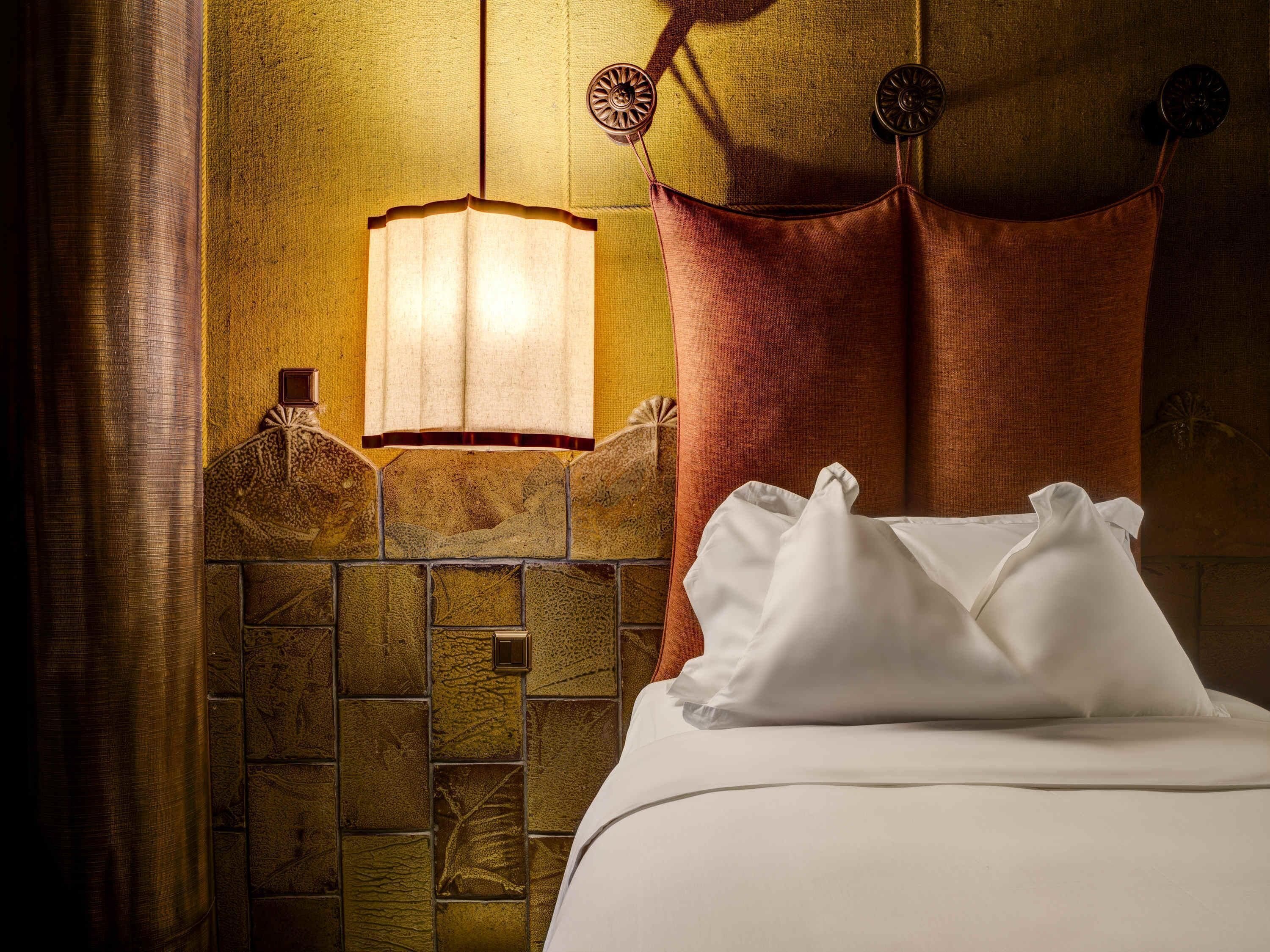 A hotel room with a bed, a wall-mounted lamp, and a textured wall.