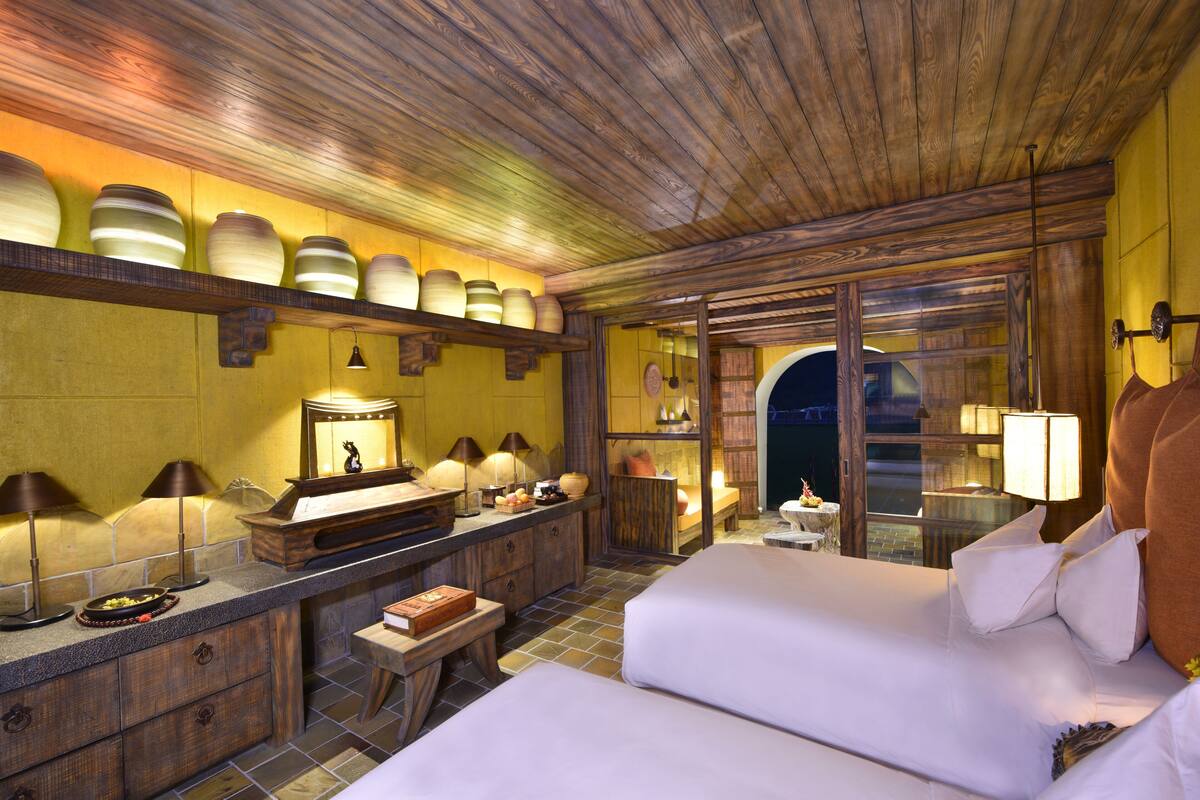 Ein Hotelzimmer mit Holzboden, einem großen Spiegel, einer hölzernen Kommode, zwei Betten und Blick durch eine Glastür.