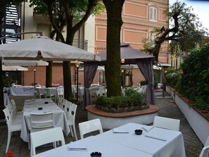 An outdoor dining area with tables and chairs, a gazebo, and a building in the background. - Hotel Casa Rossa (Montecatini Terme)