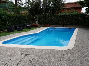 A rectangular swimming pool with a white edge, surrounded by a paved area with a few chairs and potted plants. - Hotel Casa Rossa (Montecatini Terme)