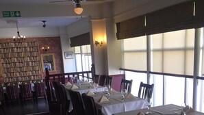 A restaurant with tables set for dining, a bookshelf, and a fire exit sign. - The George Inn (Barton-upon-Humber)