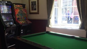 A pool table in a room with two arcade machines and a window with curtains. - The George Inn (Barton-upon-Humber)