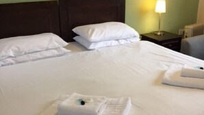 A hotel room with two beds, white linens, a framed landscape painting, a bedside lamp, and a radiator. - The George Inn (Barton-upon-Humber)