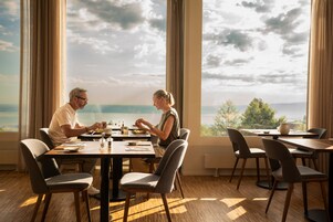 Comedor con una mesa dispuesta para dos, ventanas amplias con vista al mar y mobiliario moderno.