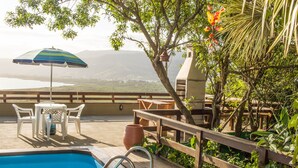 Zona de piscina con muelle de madera, mesa y sillas, y vista al paisaje.