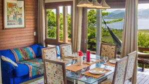 Una habitación con sofá azul, mesa de comedor, sillas y vistas a un lago y montañas.