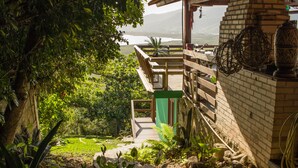 Una terraza de madera con vistas a un lago, rodeada de abundante vegetación y un edificio de ladrillo con una puerta verde.
