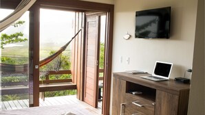 Un dormitorio con una cama, un escritorio de madera con una computadora portátil, un televisor en la pared y una hamaca afuera de un ventanal corredizo.