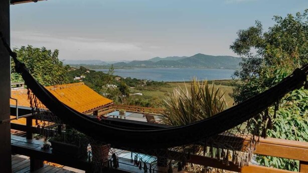 Una hamaca en una terraza de madera con vistas a un paisaje pintoresco con montañas y una masa de agua.