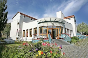 Un edificio moderno con un ingresso in vetro curvo, circondato da un giardino fiorito e ricco di colori.