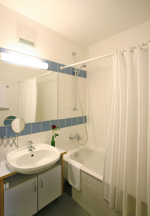 A bathroom with a white sink, mirror, and bathtub. - Am Spiegeln dialog.hotel.wien (Vienna)