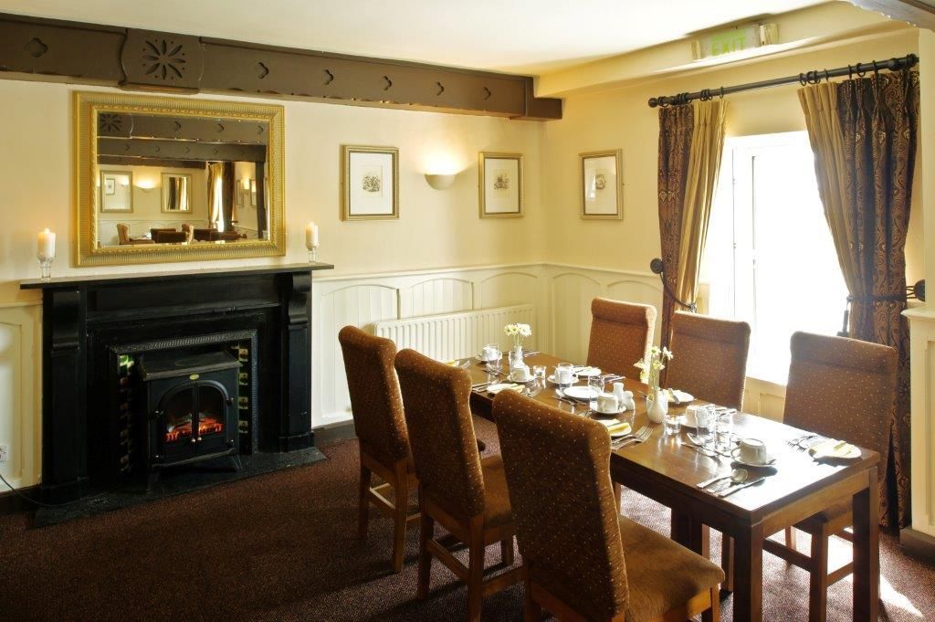 A dining room with a fireplace, a table set for four, and framed pictures on the wall.