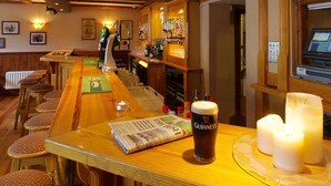 Zona de bar con taburetes, barra, un periódico, una cerveza en vaso y velas.