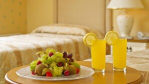 Una cama con un edredón blanco, una mesita de noche con una lámpara, y un plato de fruta junto a un vaso de zumo de naranja sobre una mesa de madera.