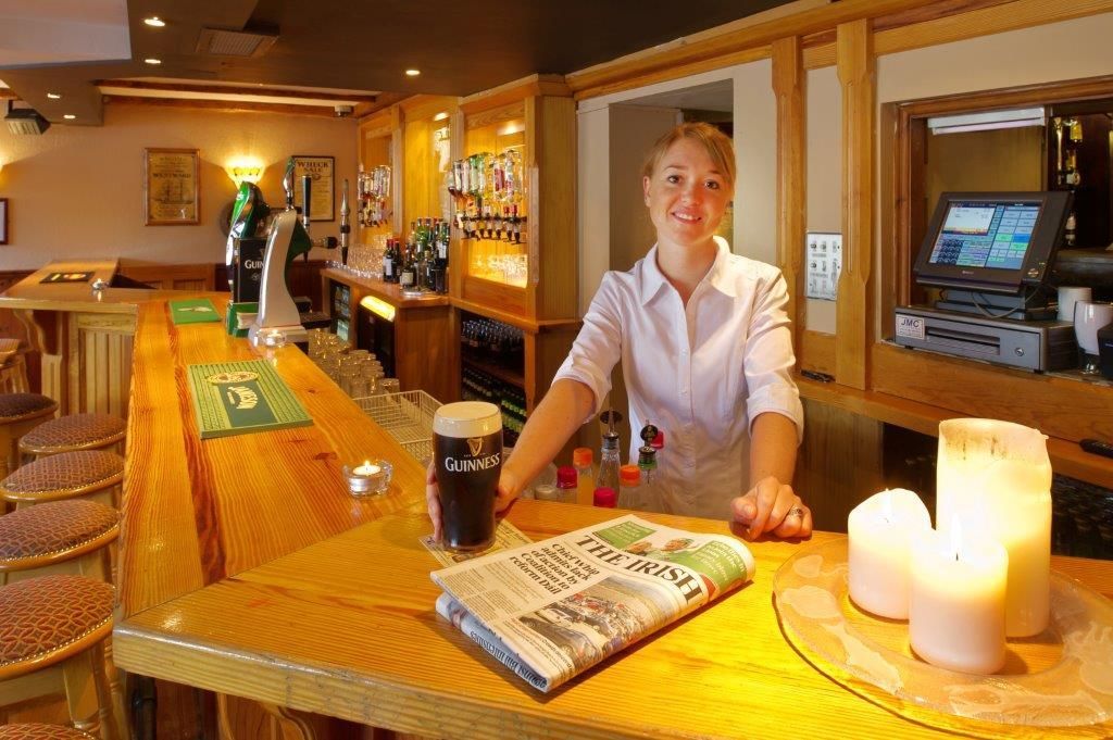 Una zona de bar con una torre de cerveza Guinness, un periódico y velas sobre la mesa.