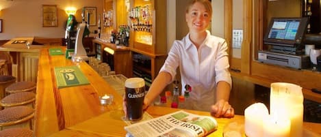 Una zona de bar con una torre de cerveza Guinness, un periódico y velas sobre la mesa.