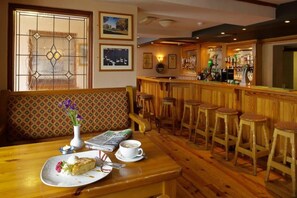 Una zona de bar con taburetes de madera, una barra y un área de estar con un banco estampado y una mesa con un plato de comida y una taza.