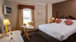 Habitación de hotel con cama, mesita de noche, lámpara, silla, ventana y una pequeña mesa con lámpara y botella.