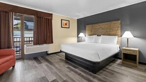 A hotel room with a bed, a nightstand, a chair, a window with curtains, and a picture on the wall. - Travelodge Rapid City (Rapid City)