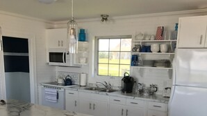 Una cocina moderna con armarios blancos, una isla de mármol y un ventanal grande.