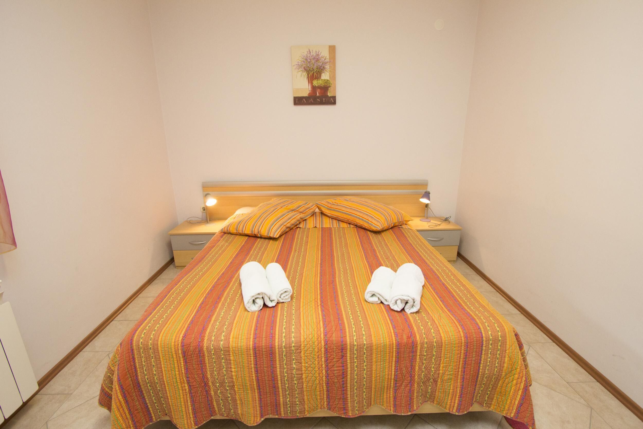 Un lit bien fait, avec une literie à rayures et deux serviettes, une table de chevet avec une lampe et un tableau accroché au mur.