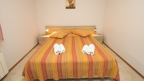 Una cama bien hecha con ropa de cama a rayas y dos toallas, una mesita de noche con lámpara, y un cuadro colgado en la pared.