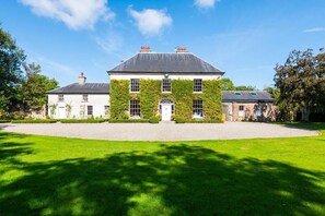 A large, white building with a grey roof, surrounded by a well-maintained lawn and trees. - Clonganny House (Cahore)