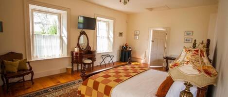 A bedroom with a large bed, a desk, a chair, a television, and a chandelier.