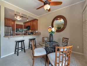 A compact kitchen with wooden cabinets, a built-in microwave, and a glass dining table with four chairs.