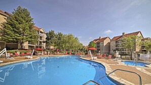 En swimmingpool med röda parasoller, solstolar och en terrass av sten.