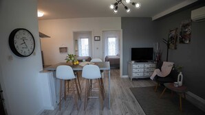 Une cuisine moderne avec un coin repas, un salon équipé d’un téléviseur et une horloge au mur.