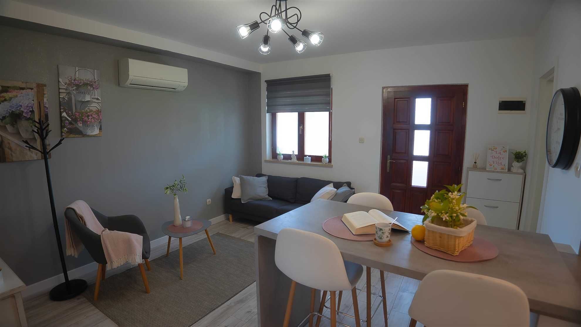 A modern living room with a sofa, a dining table with chairs, a small side table, and a large window.