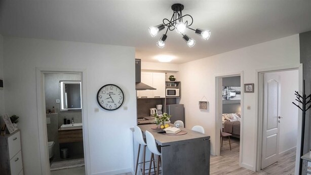 Une cuisine moderne avec un îlot central, des meubles blancs et une horloge au mur.