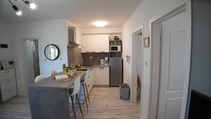 Une cuisine compacte dotée d’un îlot central, de meubles blancs, d’un four à micro-ondes et d’un réfrigérateur.