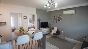 Un salon moderne comprenant un coin repas, un téléviseur à écran plat et un mur gris agrémenté d’objets décoratifs.