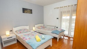 Un dormitorio con dos camas, una mesita de noche, una lámpara y una ventana con cortinas.