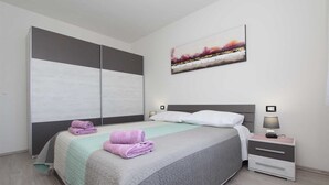 A bedroom with a bed, a nightstand, a lamp, a painting, and a wardrobe. - MONDELACO Three-Bedroom Apartment (Rovinj)
